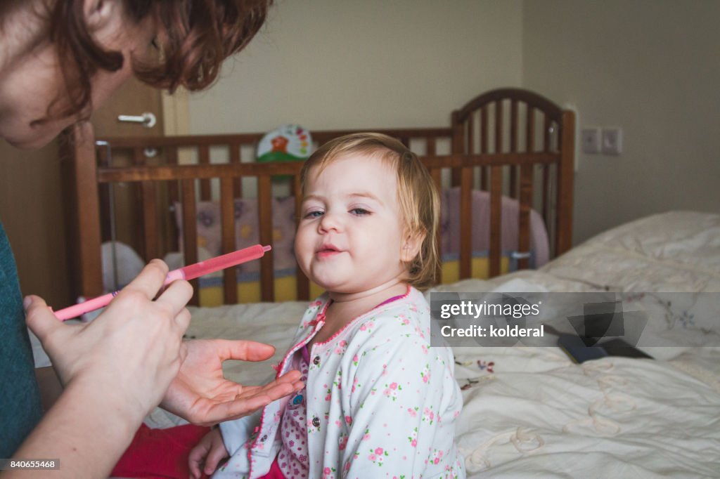 Toddler taking body temperature lowering syrup medicine