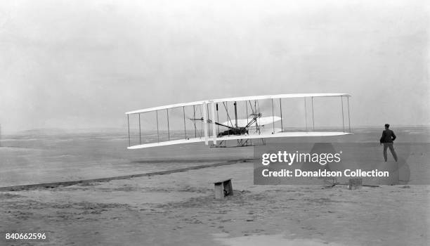 Photograph shows the first powered, controlled, sustained flight. Orville Wright at the controls of the machine, lying prone on the lower wing with...