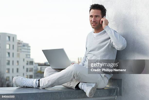 man with laptop and cellphone sitting on rooftop - philipp nemenz stock-fotos und bilder