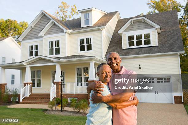 baby boomer couple hugging in front of home - senior moving house stock pictures, royalty-free photos & images