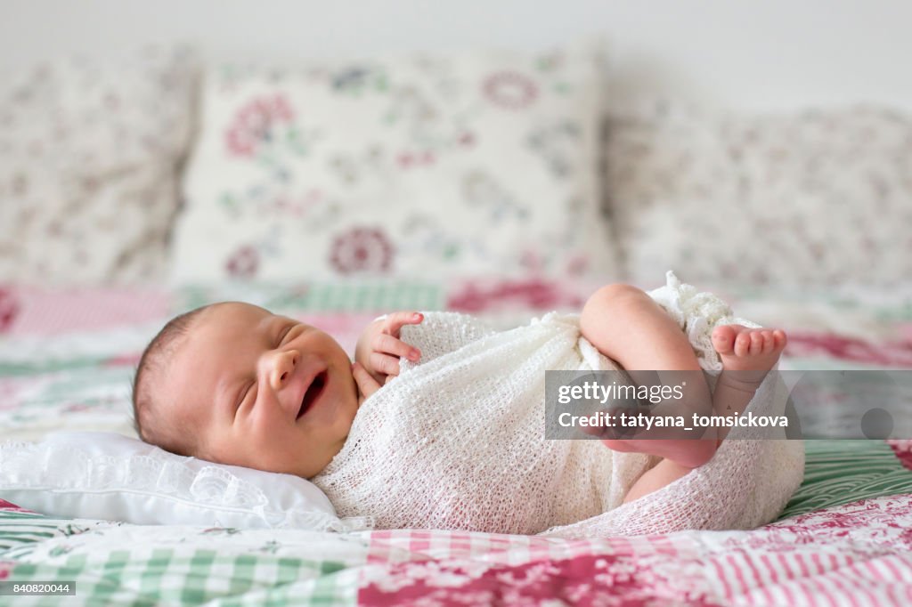 Mooie pasgeboren jongetje, breed lachend, verpakt in wrap, liggend in bed