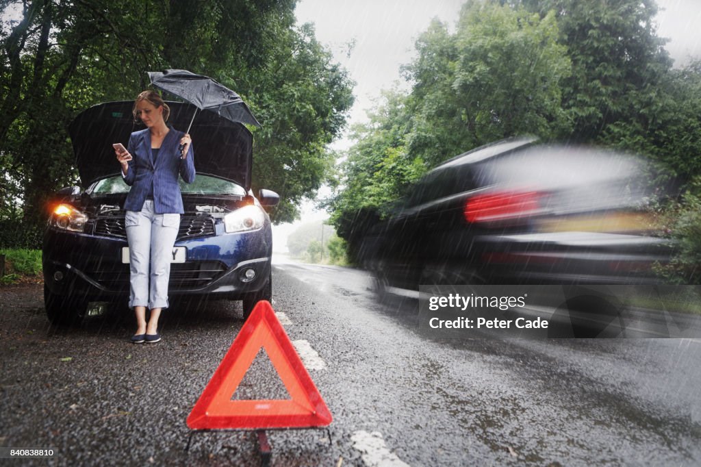 Woman on side of road with broken down car in the rain