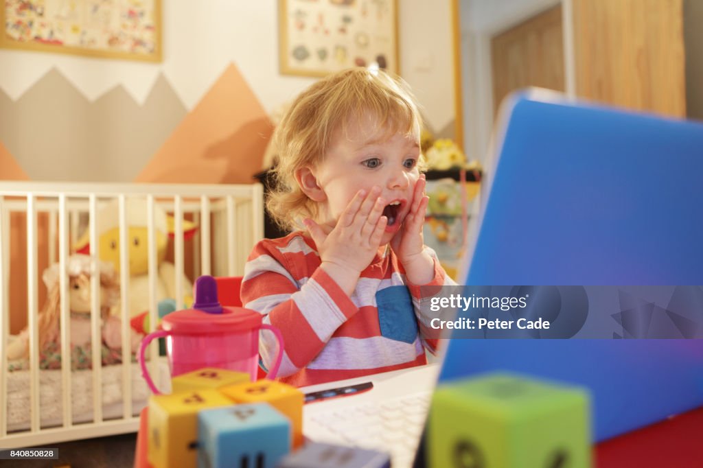 Toddler in bedroom working on laptop, looking worried