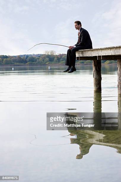 business man sitting on edge of pier, fishing - angel brinks stock-fotos und bilder