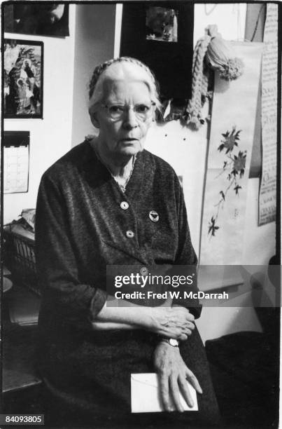 Portrait of American author, journalist, and social activist Dorothy Day as she sits on the edge of a desk in the offices of the Catholic Worker, a...