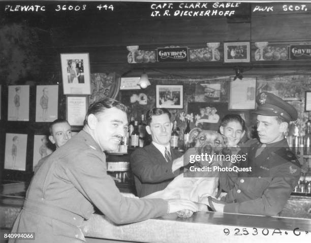 Army Air Corps Capt Clark Gable and Lt R Dieckerhoff pose with a dog and unidentified patrons at an embarkation point bar, England, 1944. The men...