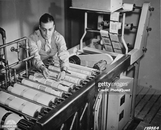 An unidentified man operates a continuous paper processing machine to develop, fix, wash, and dry paper reproductions of microfilmed v-mails at the...