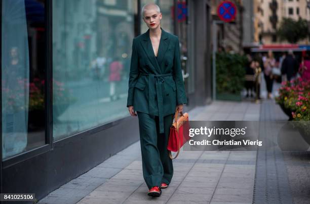 Guest wearing dark green jacket and pants, red bag outside Rodebjer on August 30, 2017 in Stockholm, Sweden.