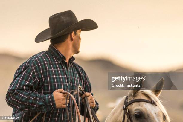 at sunset, a cowboy horseback riding on a ranch. - handsome cowboy stock pictures, royalty-free photos & images