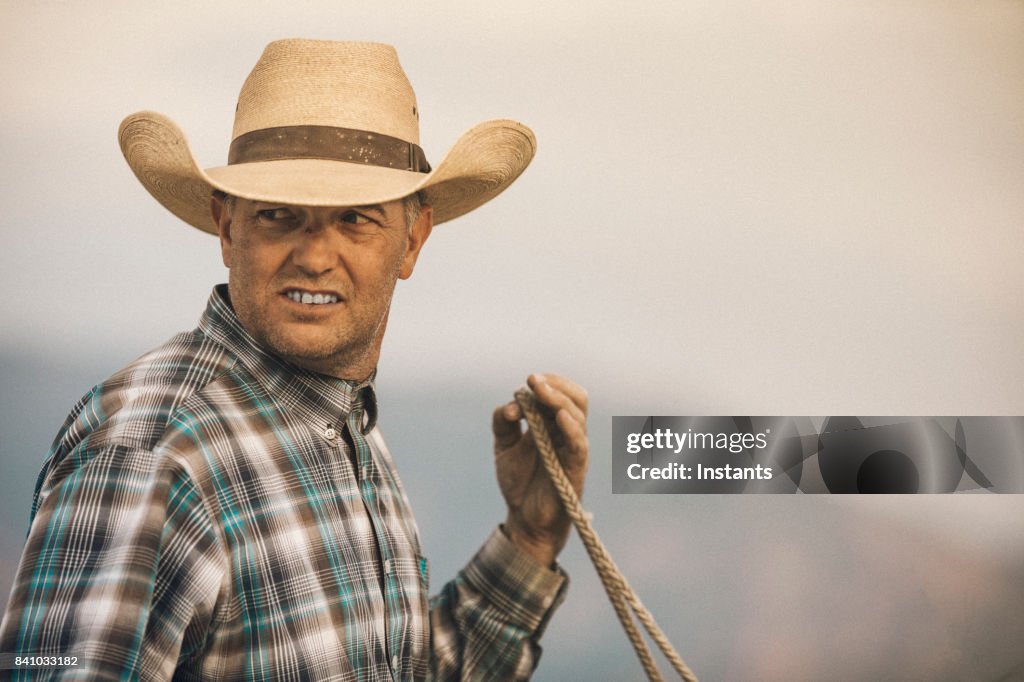 A cowboy horseback riding on a ranch at sunset, with defocused Wasatch mountains in the background.