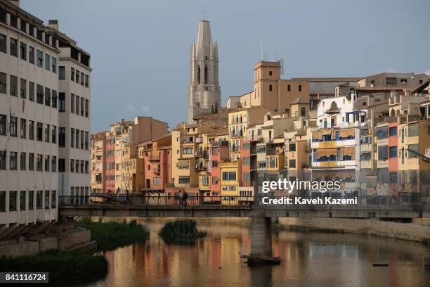 People walk on an ancient bridge over the river Onyar where in the background The Collegiate Church of St. Felix is seen behind typical houses with...