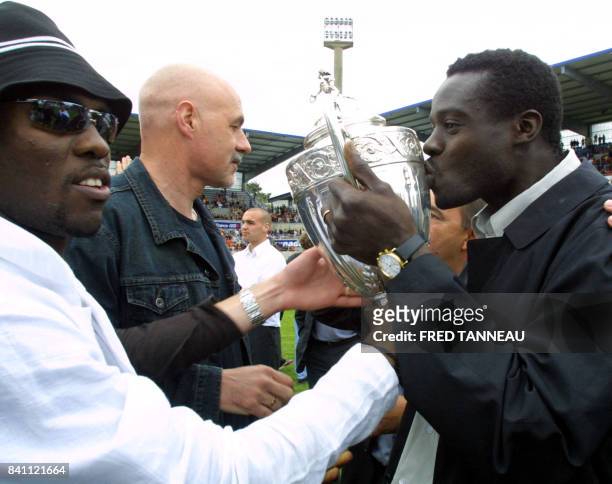 Le défenseur central sénégalais de Lorient Malik Diop , embrasse le trophée, aux côtés de son coéquipier, l'attaquant Pascal Feindouno et de...