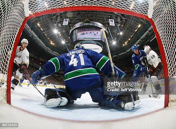 Curtis Sanford of the Vancouver Canucks slides to the right to make a save while teammate Kevin Bieksa checks Andrew Ebbett of the Anaheim Ducks...