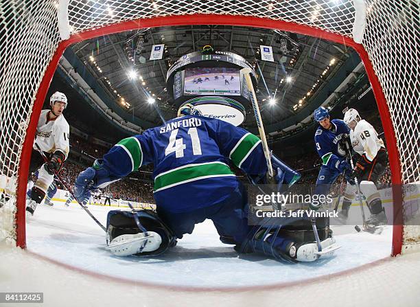 Curtis Sanford of the Vancouver Canucks slides to the right to make a save while teammate Kevin Bieksa checks Andrew Ebbett of the Anaheim Ducks...