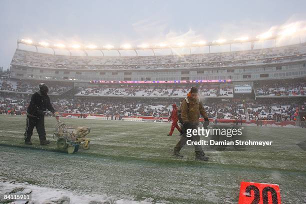 Groundskeepers clear snow off field and painting out of bounds line blue before New England Patriots vs Arizona Cardinals game. Foxboro, MA CREDIT:...