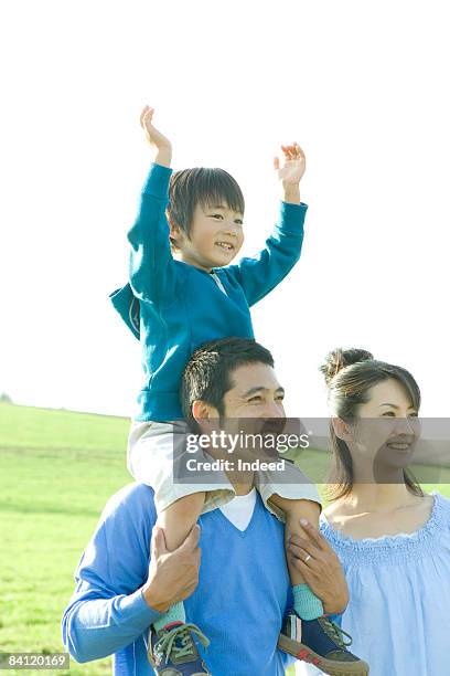 boy raising arms on father's shoulder - person auf den schultern tragen stock-fotos und bilder