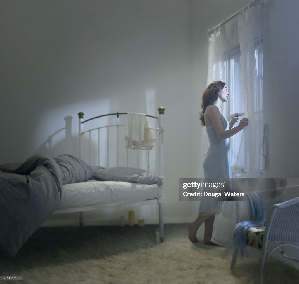 Young woman looking out of bedroom window.