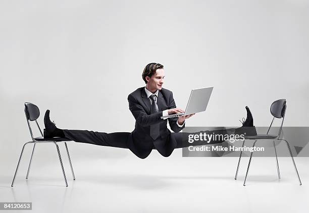 businessman balancing to two chairs holding laptop - akrobatische aktivität stock-fotos und bilder