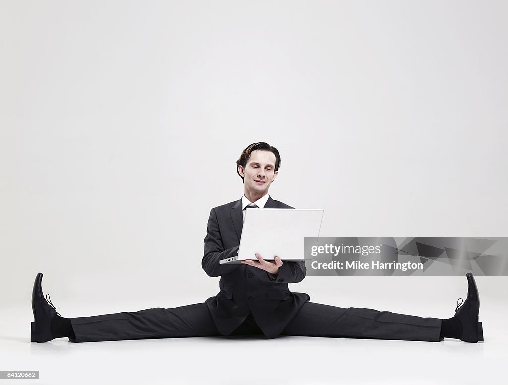 Businessman doing the splits holding laptop 