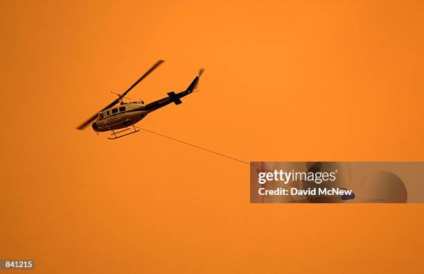 Firefighting helicopter carries a water bucket on June 24, 2002 over the town of Show Low, Arizona as smoke envelops the evacuated town. 100...