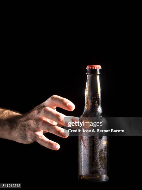 bottle of beer with the glass esmerilado with drops of water and the hands of a man grab  on a black background - beer luxury stock-fotos und bilder