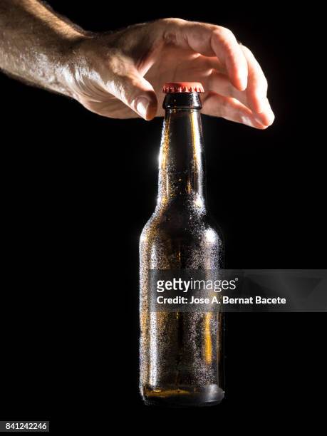 bottle of beer with the glass esmerilado with drops of water and the hands of a man grab  on a black background - beer mat stockfoto's en -beelden