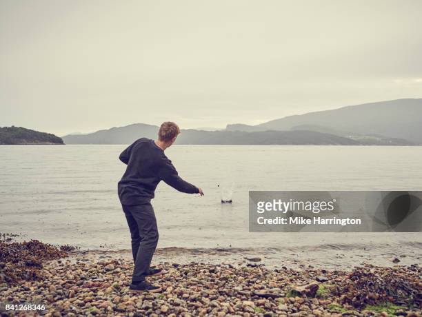 male skimming stones across lake - throwing fotografías e imágenes de stock