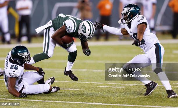 Elijah McGuire of the New York Jets jumps over Jaylen Watkins and Tre Sullivan of the Philadelphia Eagles during their preseason game at MetLife...