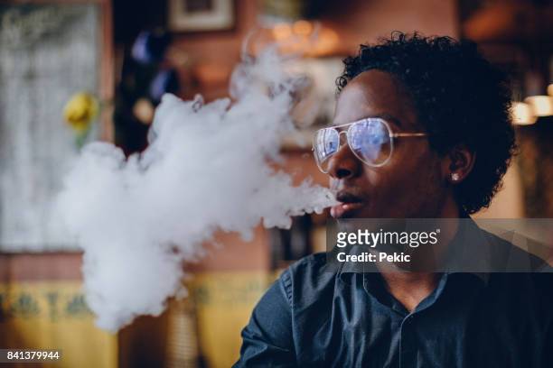 junger mann rauchen elektronische zigarette im pub - black smoke stock-fotos und bilder