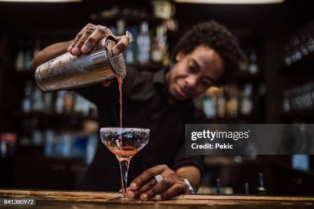 young bartender pouring cocktails in a cocktail bar - cocktail shaker stock pictures, royalty-free photos & images