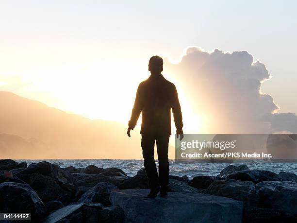 man walks on boulders towards open sea - backlit stock-fotos und bilder