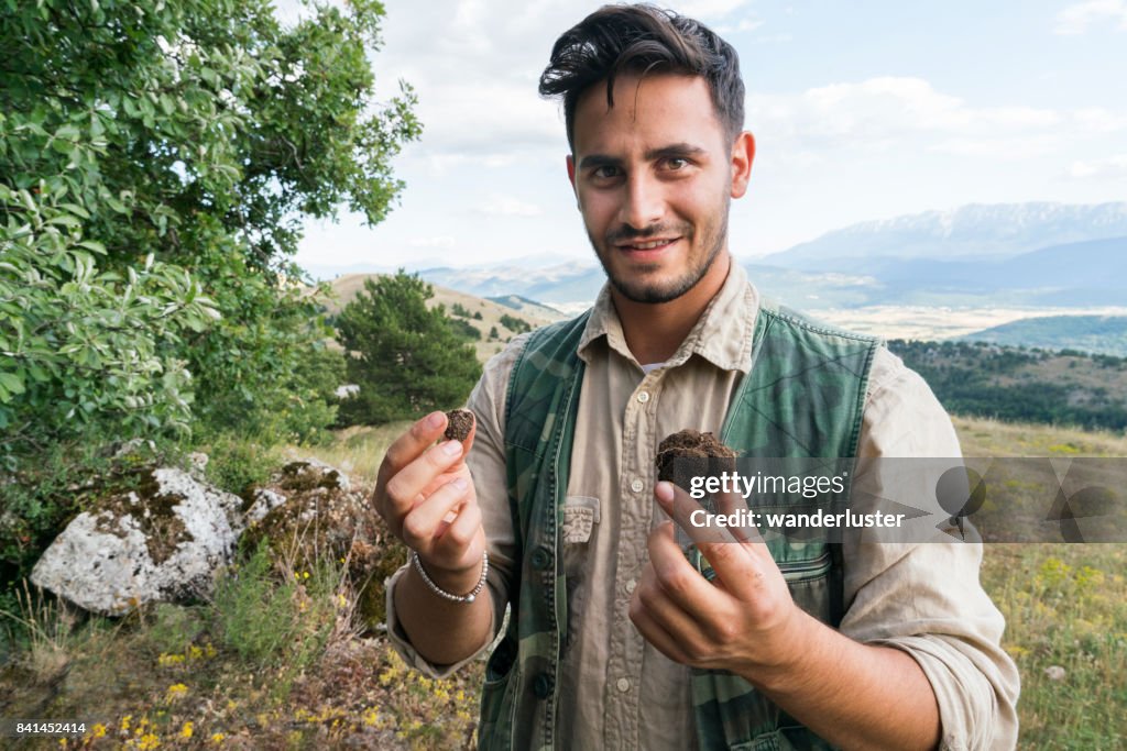 Male truffle hunter in his 20's holds a large and small truffle in his hands that he collected in the forest with his two dogs on a summer day, Abruzzo, Italy, Europe
