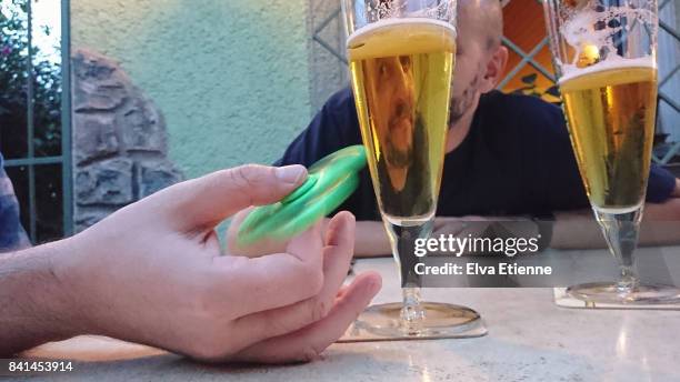 adult playing with fidget spinner whilst having a beer - fidget spinner stock-fotos und bilder