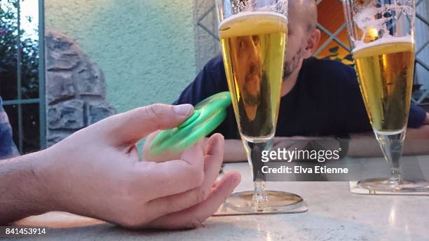 adult playing with fidget spinner whilst having a beer - fidget spinner stock pictures, royalty-free photos & images