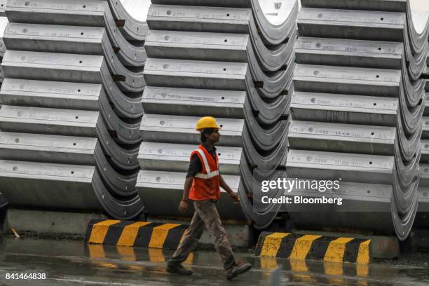 Worker walks past precast concrete tunnel segments sitting stacked outside at the Mumbai Metro Rail Corp. Casting yard in Mumbai, India, on Monday,...