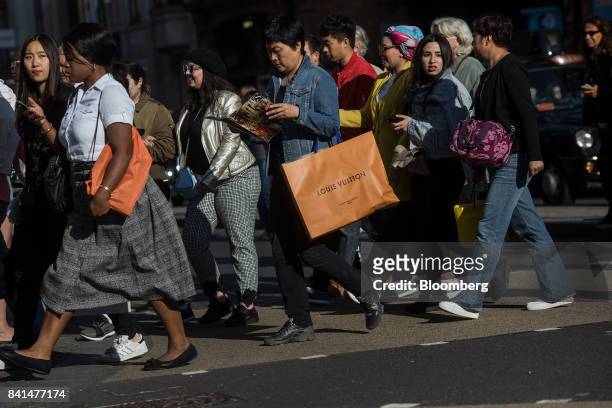 Shopper carries an LVMH Moet Hennessy Louis Vuitton SE branded shopping bag as she crosses the road with other pedestrians at Oxford Circus in...