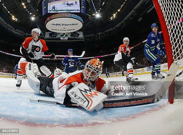Martin Biron of the Philadelphia Flyers dives to make a save while teammate Matt Carle and Jannik Hansen of the Vancouver Canucks look on during...