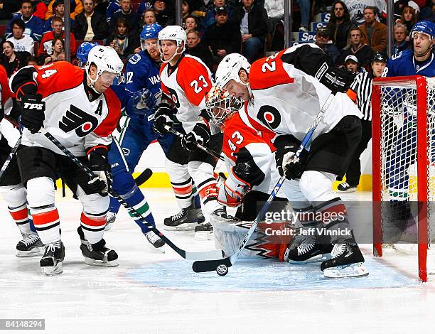 Martin Biron of the Philadelphia Flyers looks on as teammates Mike Knuble and Kimmo Timonen clear a rebound off a Vancouver Canucks shot during their...