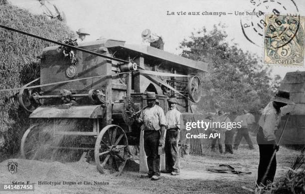 Carte postale illustrée par la photographie d'agriculteurs travaillant avec une batteuse dans un champ, en France.