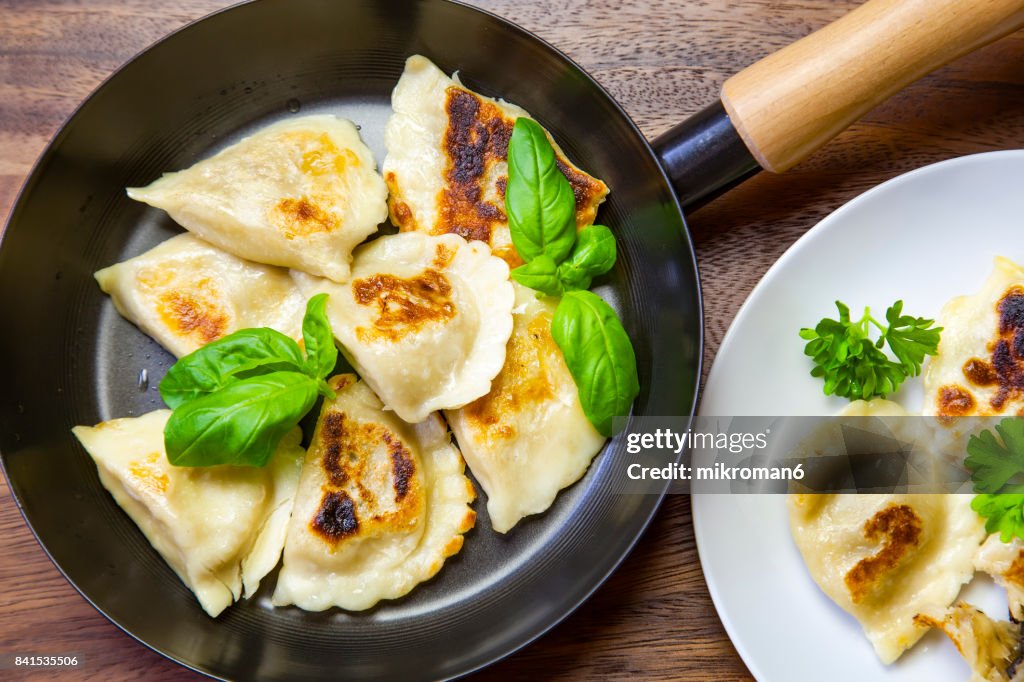 High Angle View Of Dumplings On  frying pan and white Plate (Polish pierogies)