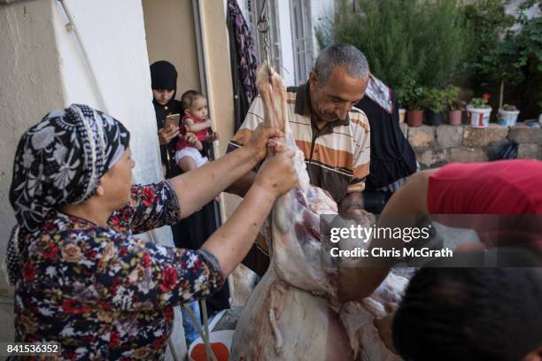 Syrian refugee Husin Lok is helped by family members to cut the meat off a sacrificial sheep at their home during Eid-al-Adha celebrations on...