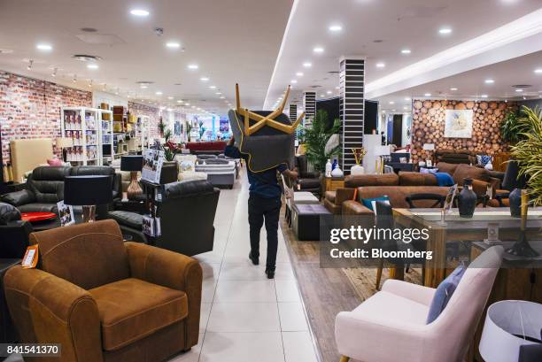 An employee carries a chair past displays of home furnishings inside a Rochester furniture store, operated by Steinhoff International Holdings NV, in...