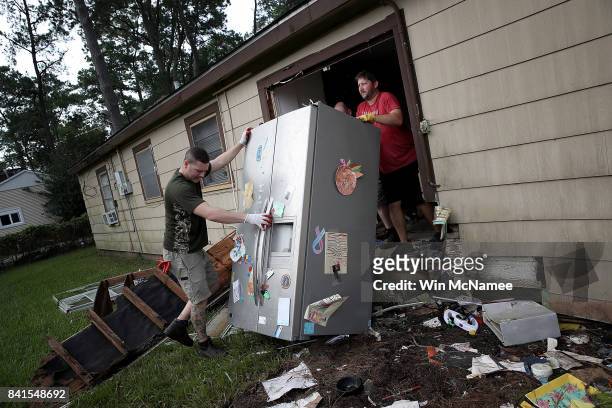 Chris Gaspard and Derek Pelt help remove a refrigerator and other ruined items from their friend Bryan Parson's home following flooding in the wake...