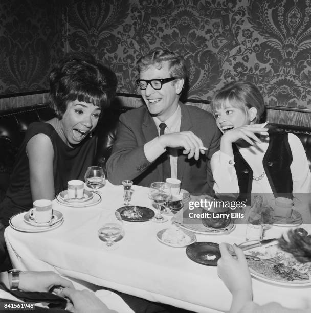 Welsh singer Shirley Bassey, English actor Michael Caine and Anglo-Hungarian fashion designer Edina Ronay laugh together while sitting at a table at...