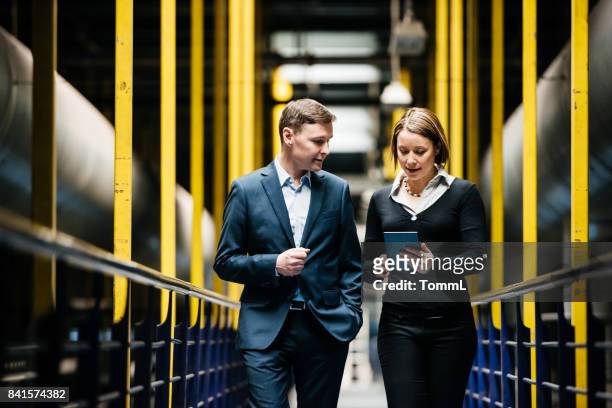 two business person walking a dark factory hallway - factory stock pictures, royalty-free photos & images