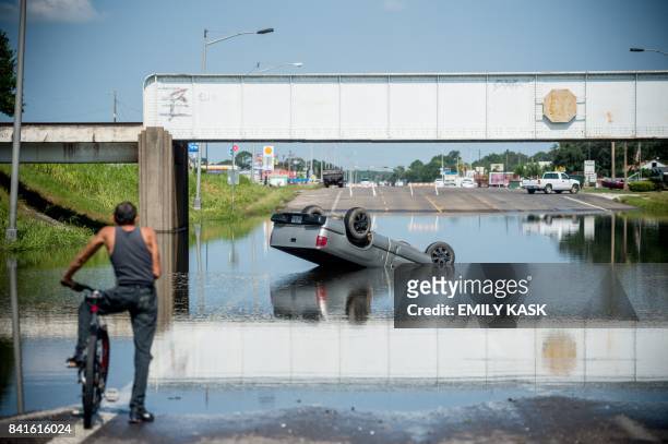 Bicyclist looks at a truck flipped into floodwater in Port Arthur, Texas on September 1, 2017. - Houston was limping back to life on Friday one week...