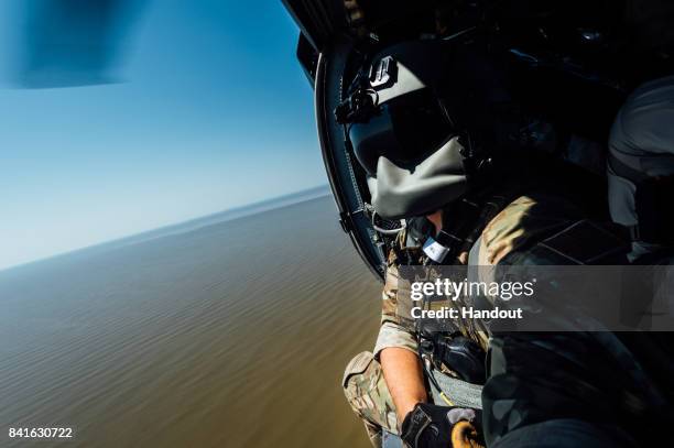 In this U.S. Air Force handout, Senior Airman Austin Hellweg, 129th Rescue Squadron special missions aviator, looks out the side door of a HH-60...