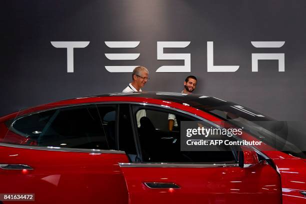 Two man stand in front of a Tesla logo behind the Tesla Model S at the electric carmaker Tesla showroom of El Corte Ingles store in Lisbon, on...