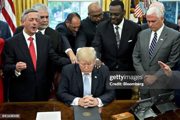 President Trump, center, bows his head during a prayer while surrounded by U.S. Vice President Mike Pence, right, faith leaders and evangelical...