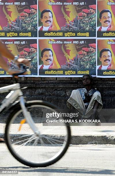 Sri Lankan cyclist rides past an elderly man sitting under posters on a street in Colombo on January 4 featuring an image of Sri Lankan President...